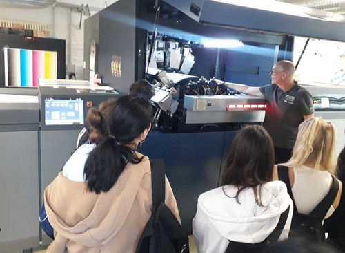 Schülerinnen vor einer großen Maschine in einer Druckerei. 