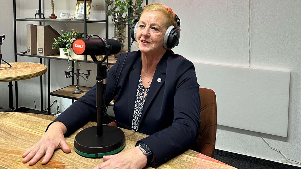 Eine Frau sitzt im Studio mit Kopfhörern an einem Mikrofon.