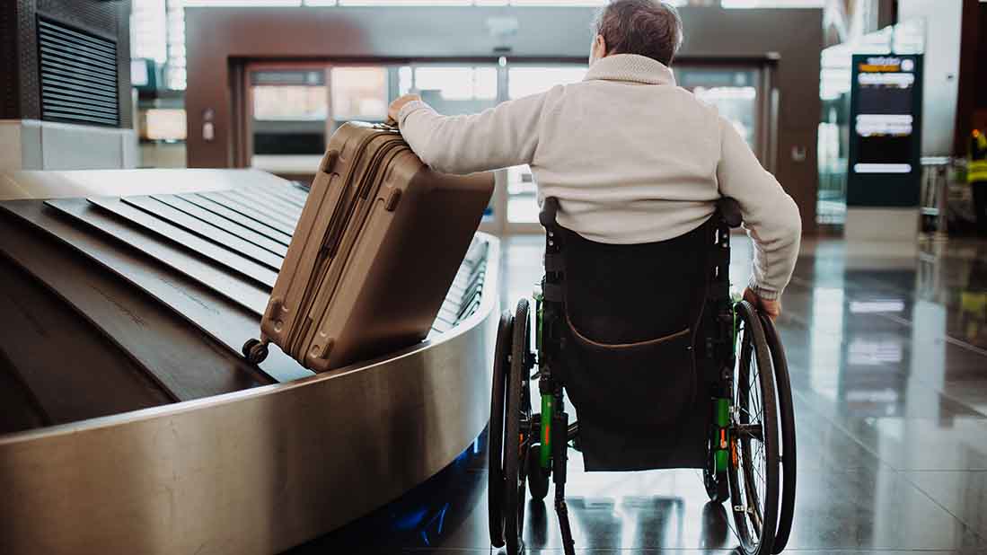 Mann im Rollstuhl holt Koffer vom Gepäckband