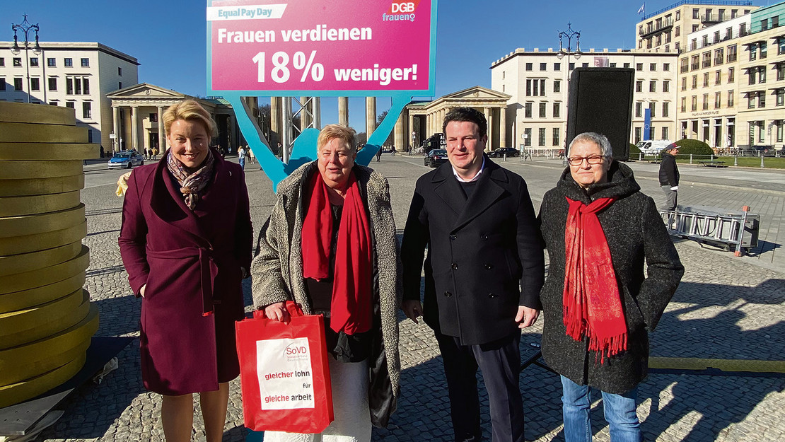 Vier Personen und stehen vor einem Transparent mit der Aufschrift "Frauen verdienen 18 Prozent weniger!"