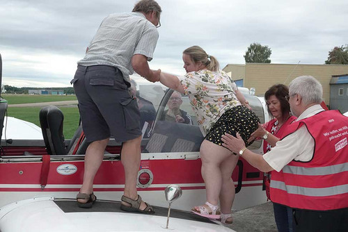 Drei Personen helfen Frau mit Behinderung in ein kleines Flugzeug. 