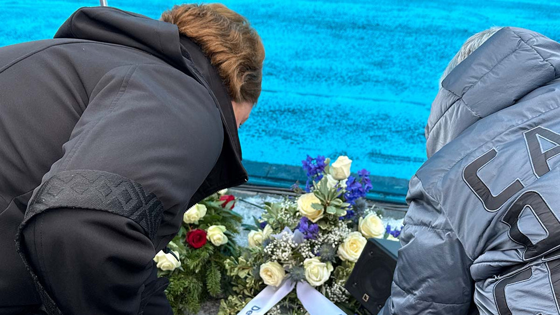 Zwei Frauen knien und legen einen Kranz ab. 