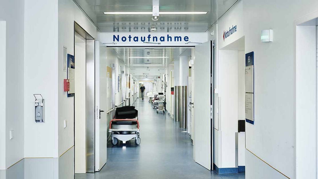 Blick in den Flur eines Krankenhauses, oben ein Wegweister zur Notaufnahme. 