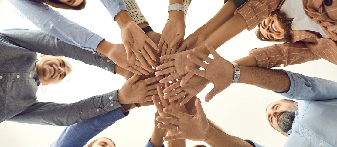 Menschen stehen in einem Kreis und halten ihre Hände in der Mitte zusammen. 