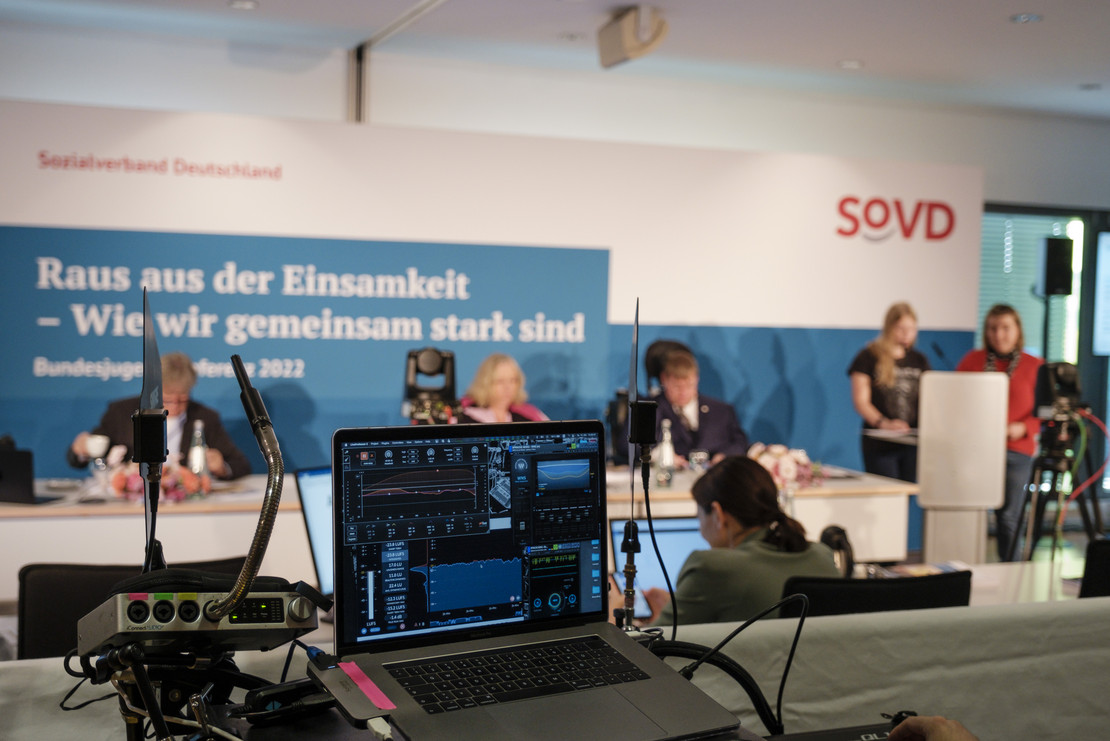 Blick auf Laptop, dahinter unscharf Podium der Bundesjugendkonferenz