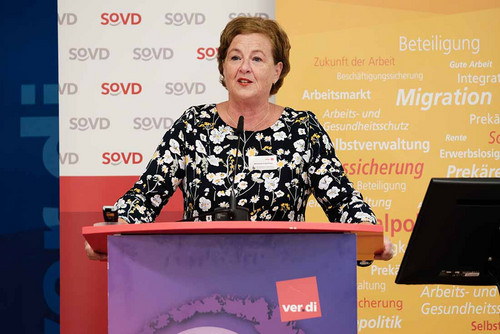 Frau spricht an einem Pult ins Mikrofon.