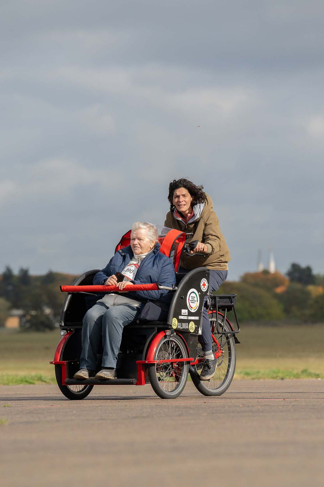 Eine Frau fährt ein Lastenfahrrad, in dem eine ältere Frau vorne sitzt. 