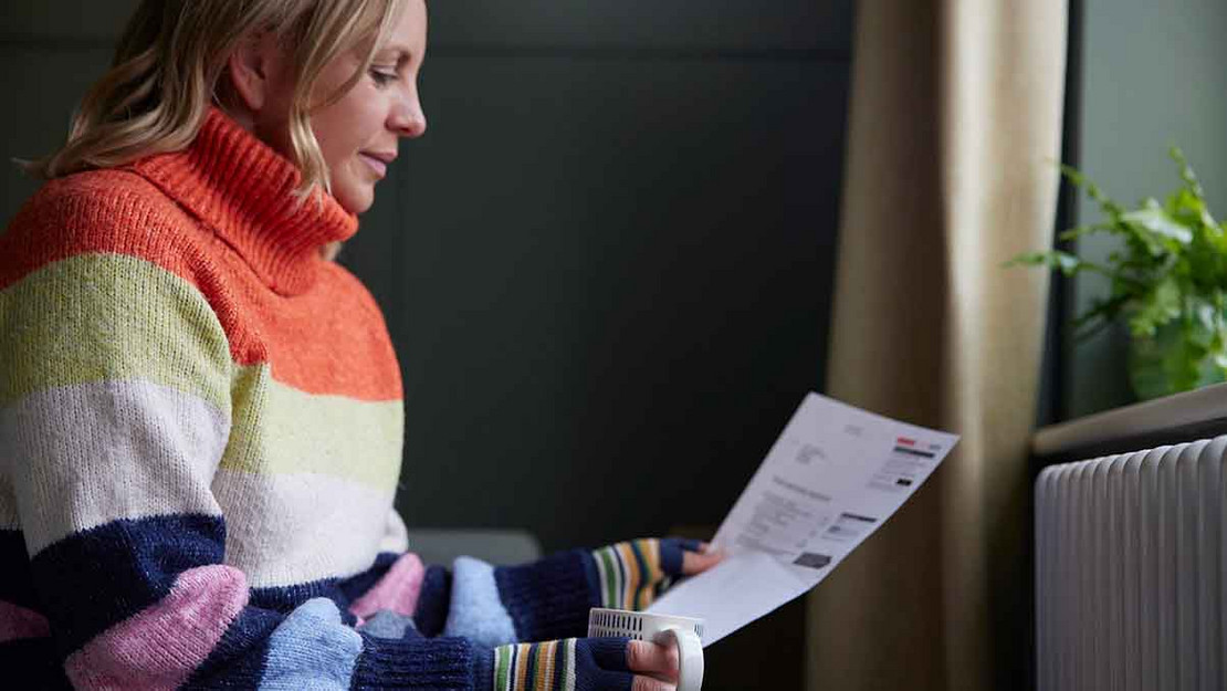 Frau im dicken Pullover liest auf einem Blatt Papier. 