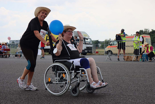 Frau schiebt Frau im Rollstuhl, die einen Luftballon in der Hand hält. 