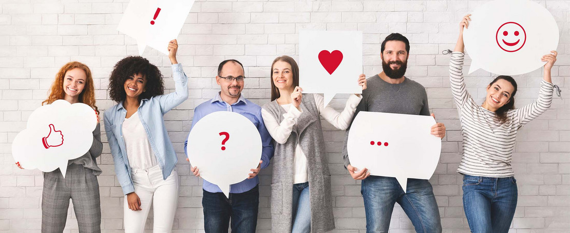 Gruppe von Menschen steht vor einer Mauer und hält Sprechblasen. 