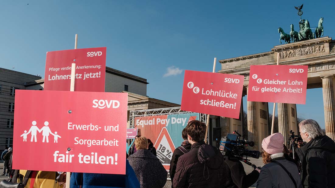 Menschen tragen rote Plakate mit politischen Forderungen vor dem Brandenburger Tor. 