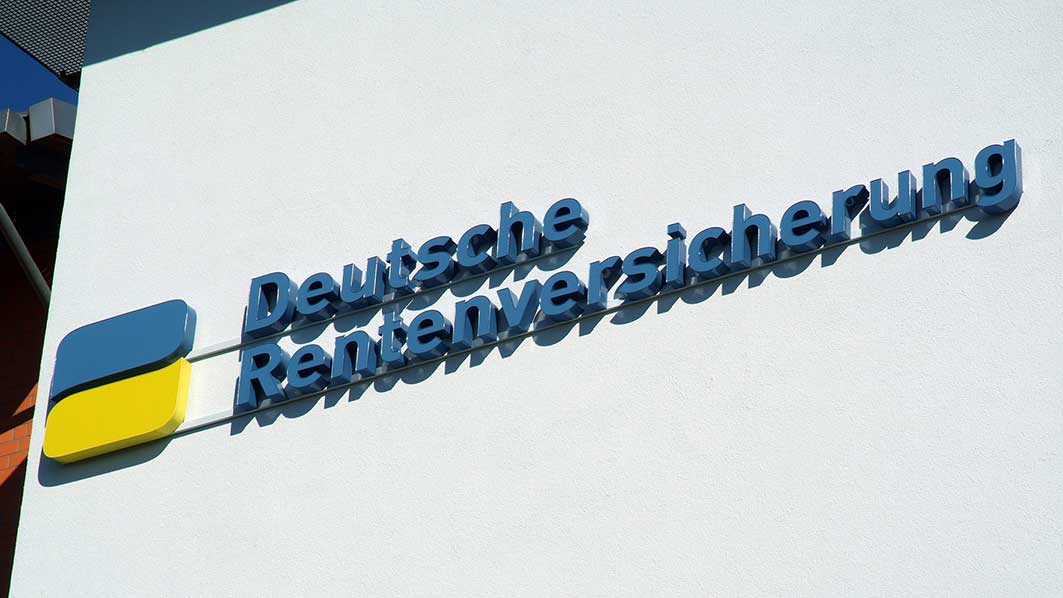 Blau-gelbes Logo und Schriftzg "Deutsche Rentenversicherung" an einer Häuserwand. 