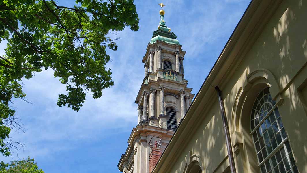 Berliner Sophioenkirche vor blauem Himmel mit einem grünen Baum davor. 