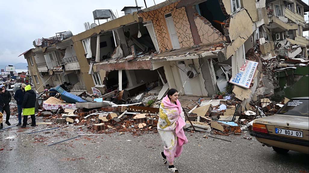 Frau läuft vor einem zerstörten Haus. 