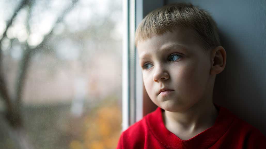 Kind blickt traurig durch eine Fensterscheibe. 